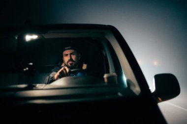 Adam gece araba sürerken yalnızdır. Genç, ciddi odaklanmış bir adam gece geç saatte araba sürüyor.