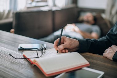 Psikoterapist ve hasta ofiste bir randevuda. Doktor 'un elleri not defterini yakın çekimde. Doktor müşterinin geçmişini kaydediyor. Bir erkek hasta, büyük, parlak bir ofiste, bir kanepede yatıyor.