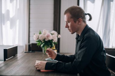 Genç bir adam masadaki bir deftere yazar. Gazeteci, yazar notlar alır, işyerindeki yazılar üzerinde çalışır.