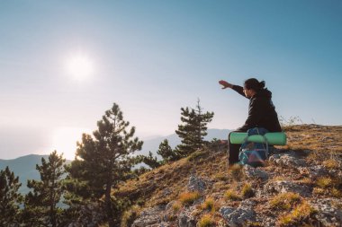 Gün doğumunda dağın tepesinde sırt çantalı bir erkek turist. Kamp malzemeleriyle genç yakışıklı adam sabah güneşini sevinçle karşılıyor dağlarda
