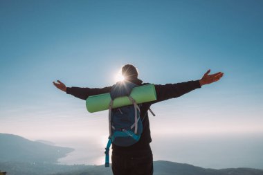 Gün doğumunda bir turist kollarını bir dağın tepesine uzatarak ayakta durur. Turist ekipmanlı genç adam neşeyle karşılıyor denizi gören dağlarda sabah güneşini.
