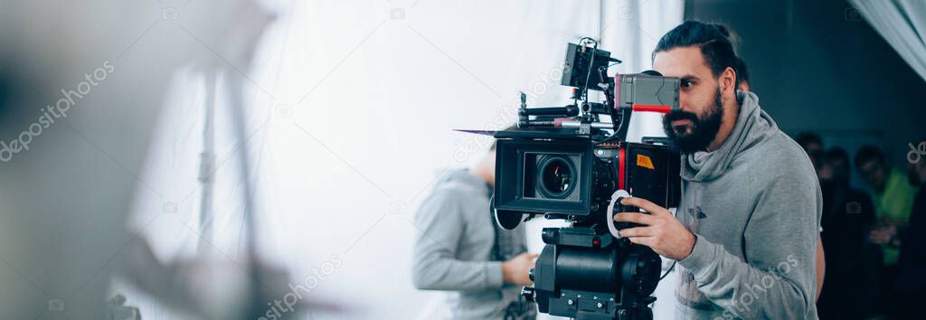 Director of photography with a camera in his hands on the set. Professional videographer at work on filming a movie, commercial or TV series. Filming process indoors, studio