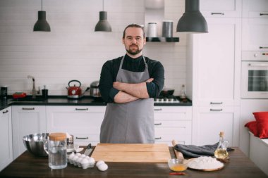 Erkek bir aşçı mutfakta evde yemek pişiriyor. Mutfağındaki önlüklü genç adam yemek pişirmek için gerekli malzemelerle birlikte masada.