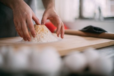 Erkek bir şef mutfakta erişte hamuru hazırlar. Un ve hamurla ellerini kapat. Mutfağındaki önlüklü genç adam masanda erişte pişirmek için malzemelerle bekliyor.