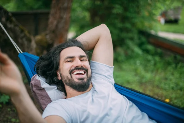 A man rejoices and laughs while lying in a hammock. Close-up. A young guy lies in a hammock, rejoices in the fresh air in the summer in the green of trees in the country