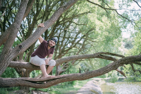 Молодой Человек Сидит Дереве Парке Красивый Парень Летней Одежде Босиком — стоковое фото