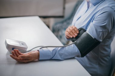 Eller masanın üzerinde bir tonometre ile. Gömlekli bir kadın elektronik tonometreyle kan basıncını ölçer.