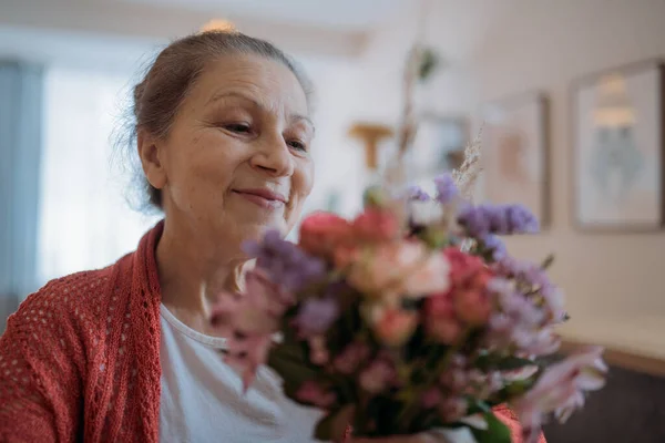 Portrait of an elderly woman holding flowers. Beautiful aged woman with a bouquet at home on a holiday
