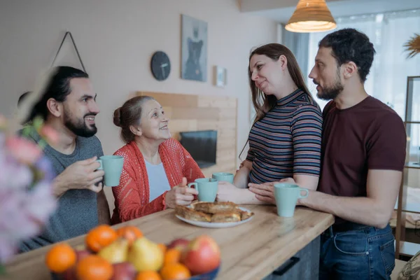 Children congratulate mom on the holiday, family feast. Adult brothers and sister have fun drinking tea with an elderly beautiful mother in the kitchen. A family visiting their beloved mother on a holiday