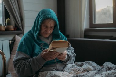 Büyükannem kanepede oturuyor ve kitap okuyor. Yaşlı bir kadın, bir emekli, gün boyunca oturma odasında dinleniyor. Yatağın yanında yürüyenler