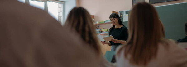 Учитель преподаёт урок в школе. Молодая женщина учитель на уроке в классе на доске объясняет урок для детей