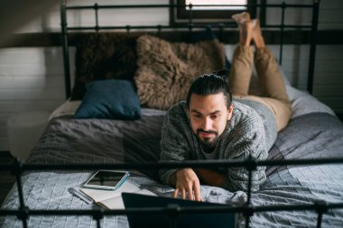 Genç adam evde dizüstü bilgisayarla yatakta yatıyor. Yakışıklı, rahat, Kafkasyalı bir adam çalışır, çalışır, gündüzleri rahat bir yatakta yatak odasında internette sörf yapar.