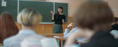 Öğretmen okulda bir ders veriyor. Karatahta sınıfındaki genç bayan öğretmen çocuklara bu dersi açıklıyor.