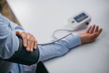 Eller masanın üzerinde bir tonometre ile. Gömlekli bir kadın elektronik tonometreyle kan basıncını ölçer.