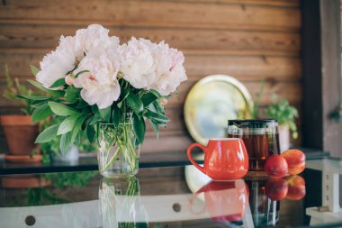 Çay aksesuarları ve çiçeklerle dolu bir hayat. Çaydanlık, çay fincanları ve parlak bir günde cam bir masanın üzerinde şakayık demeti