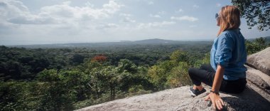 Bir kadın bir dağın yamacında oturur ve ufka bakar. Genç kız yukarıdan tropikal adanın manzarasının tadını çıkarıyor.