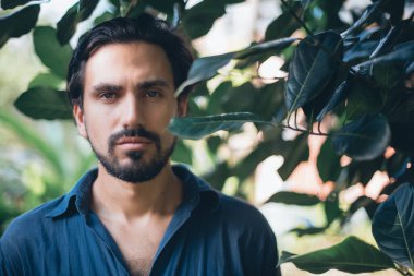 Yeşil yapraklı bir adamın kavramsal portresi. Güzel esmer adam, tropik çalıların arasında poz veren bir model. Yakın plan.