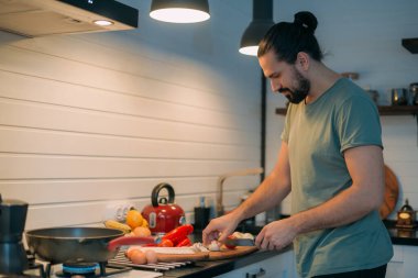 Bir adam mutfakta kahvaltı hazırlar. Genç beyaz erkek, büyük, parlak bir mutfakta, gaz sobasında öğle yemeği için yemek hazırlıyor.