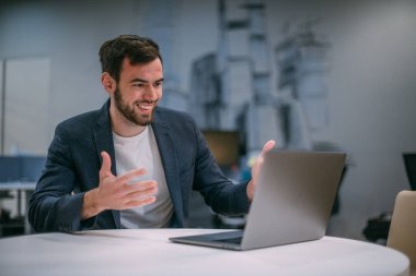 İş bilgisayarında genç ve mutlu bir iş adamının portresi. Genç yakışıklı bir adam bilgisayarın başına oturur ve modern bir ofisin içinde başarının tadını çıkarır.