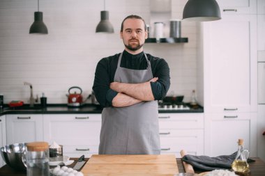 Erkek bir aşçı mutfakta evde yemek pişiriyor. Mutfağındaki önlüklü genç adam yemek pişirmek için gerekli malzemelerle birlikte masada.