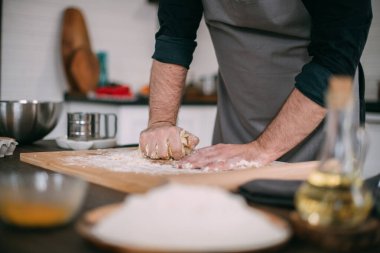 Erkek bir şef mutfakta erişte hamuru hazırlar. Un ve hamurla ellerini kapat. Mutfağındaki önlüklü genç adam masanda erişte pişirmek için malzemelerle bekliyor.