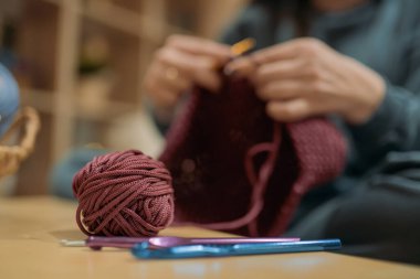 Genç kadın oturma odasındaki kanepeye bir sepet örüyor. Elleri yakın çekim. Hobisi için güzel bir kız. Akşamları evde kordondan örgü örüyor.