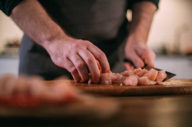 Erkek bir şef mutfakta taze et hazırlar. Ellerinizi bir bıçak ve bir parça etle kapatın. Evdeki mutfakta önlüklü genç adam et tabağı pişirmek için gerekli malzemelerle birlikte.