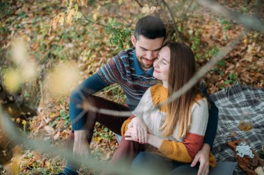 Gölde piknik yapan sevgi dolu bir çift. Genç bir adam ve kadın, sonbaharda parktaki su kenarında bir battaniyenin üzerinde şarap ve meyvelerle otururlar. Genç bir aile yıldönümünü kutluyor..