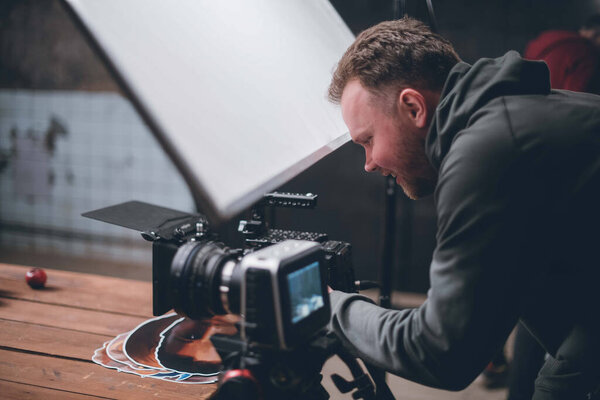 Director of photography with a camera in his hands on the set. Professional videographer at work on filming a movie, commercial or TV series. Filming process indoors, studio