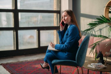 Modern ofis içinde iş kadını portresi. Mavi takım elbiseli şık bir genç kız telefonda konuşuyor. İş kadını, bir iş kadını portresi..