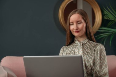 Modern ofis içinde dizüstü bilgisayarla iş kadını portresi. Kanepede dizüstü bilgisayarı olan iş elbisesi giymiş şık bir genç kız. İş kadını, bir iş kadını portresi..