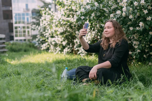 Женщина Сидит Траве Телефоном Большом Городском Парке Молодая Пухленькая Симпатичная — стоковое фото