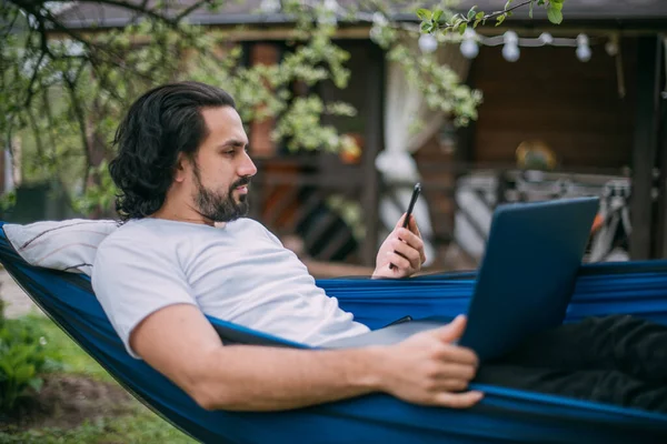 Een Man Werkt Met Een Laptop Een Telefoon Een Hangmat — Stockfoto