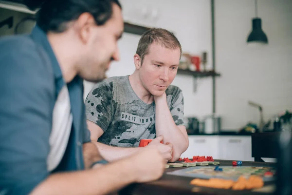 Friends play a board game in the living room. The company of young guys sits at a table and emotionally and cheerfully plays a card game on the weekend