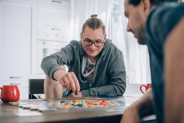 Friends play a board game in the living room. The company of young guys sits at a table and emotionally and cheerfully plays a card game on the weekend