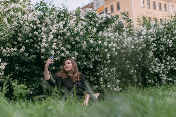 Женщина Сидит Траве Телефоном Большом Городском Парке Молодая Пухленькая Симпатичная — стоковое фото