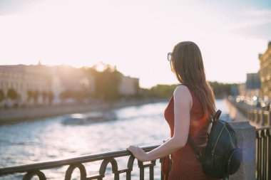Yazın gün batımında nehrin kenarında genç ve güzel bir kadının portresi. Bir kız akşamüstü nehir kıyısındaki bir Avrupa kasabasında gün batımında yürür.