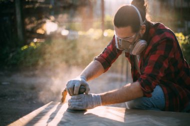 Erkek bir marangoz odun öğütücüsüyle çalışır. Profesyonel ekipmanlar ve koruyucu ekipmanlar. Genç profesyonel zımpara ahşap masa..