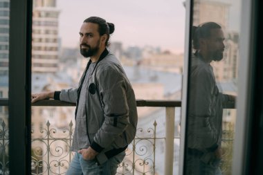 Penceredeki şehre bakan genç yakışıklı bir adamın portresi. Şehir hayatı. Uzun saçlı beyaz adam evinin ya da ofisinin geniş açık penceresinin yanında duruyor.