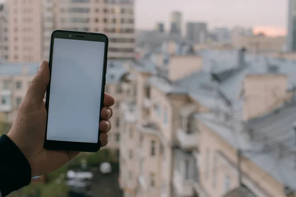 The telephone in men\'s hands against the background of the city landscape. Close-up. Male hands are holding a smartphone. Against the background of the roofs of houses. Green screen.