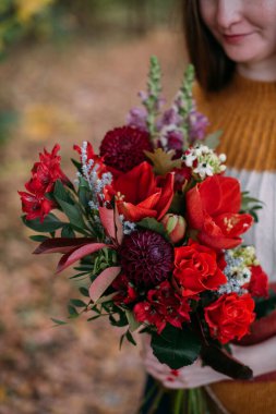 Parkta elinde bir buket çiçekle güzel bir kadının portresi. Elinde bir buket kırmızı çiçek tutan kız sonbahar doğasının arka planında
