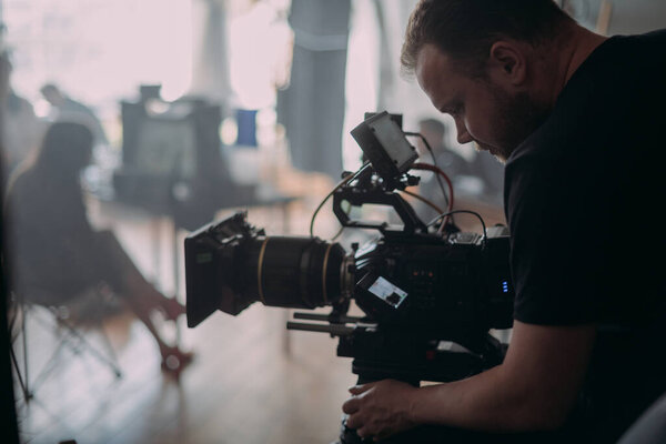 Director of photography with a camera in his hands on the set. Professional videographer at work on filming a movie, commercial or TV series. Filming process indoors, studio