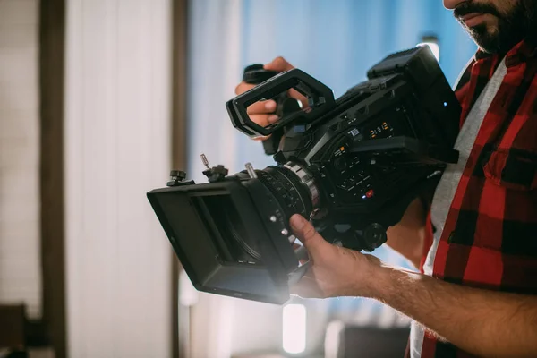 Director of photography with a camera in his hands on the set. Professional videographer at work on filming a movie, commercial or TV series. Filming process indoors, studio