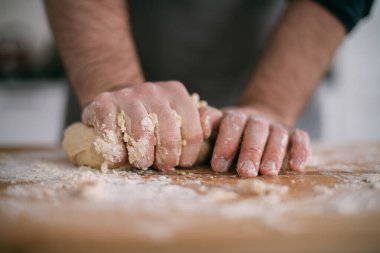 Erkek bir şef mutfakta erişte hamuru hazırlar. Un ve hamurla ellerini kapat. Mutfağındaki önlüklü genç adam masanda erişte pişirmek için malzemelerle bekliyor.
