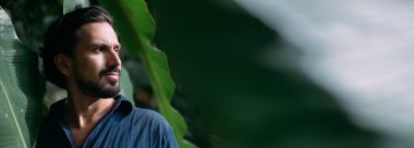 Büyük muz yaprakları içinde bir adamın kavramsal portresi. Tropik çalılıkların arasında poz veren yakışıklı bir adam. Yakın plan.