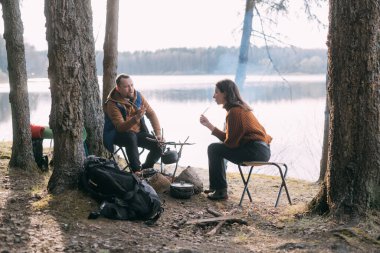 Evli bir çift gölün kıyısında çadırlı şekerlemeleri kızartıyor. Ormanda şenlik ateşiyle yürüyüş kampı. Kadın ve erkek, ateşin yanında sıcak içeceklerle sessizliğin tadını çıkarırlar.