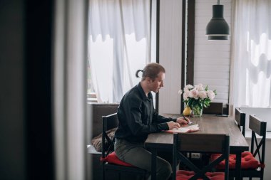 Genç bir adam masadaki bir deftere yazar. Gazeteci, yazar notlar alır, işyerindeki yazılar üzerinde çalışır.