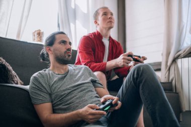 Çocuklar kanepede video oyunu oynuyorlar. Elinde joysticklerle iki genç adam büyük bir hevesle bir konsolda oyun oynuyorlar.