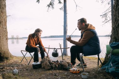 Evli bir çift gölün kıyısında çadırlı şekerlemeleri kızartıyor. Ormanda şenlik ateşiyle yürüyüş kampı. Kadın ve erkek, ateşin yanında sıcak içeceklerle sessizliğin tadını çıkarırlar.