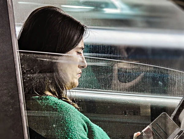 Profile of woman looking at mobile phone in car on a blurred background